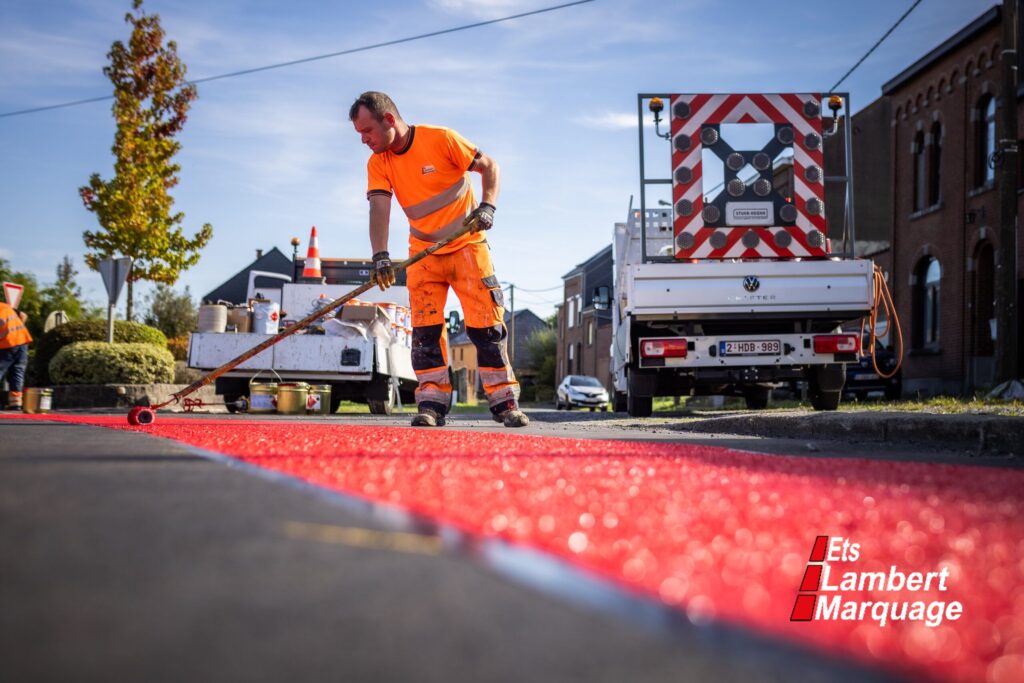 Application manuelle d’un marquage routier rouge sur chaussée par Lambert Marquage